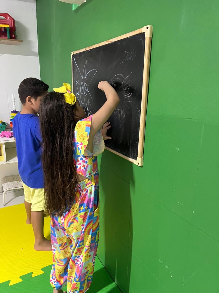 Crianças desenhando na lousa do espaço terapêutico