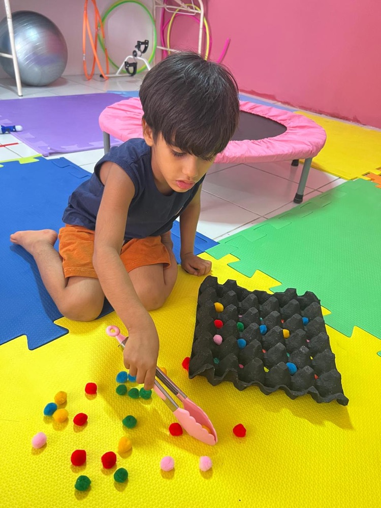 Criança em atividade sensorial com pompons coloridos na sala de terapia